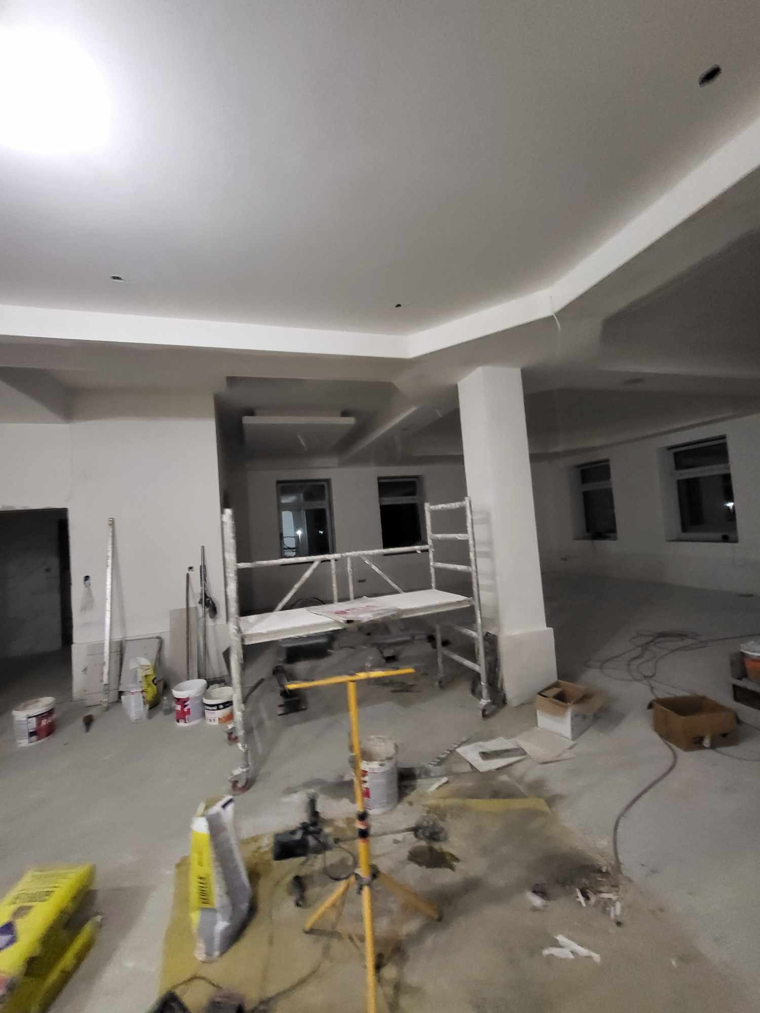 Wnętrze w trakcie prac wykończeniowych: widoczne rusztowanie, worki z zaprawą, puszki z farbą, świeżo pomalowany sufit z charakterystycznymi załamaniami i kolumnami.