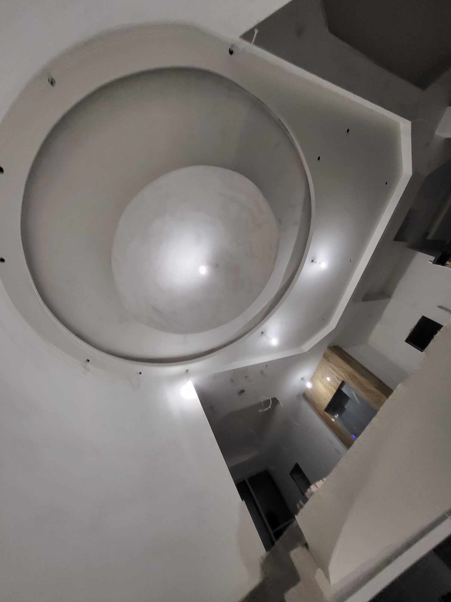 Nowoczesny sufit z płyty gipsowo-kartonowej z okrągłym wgłębieniem i punktowym oświetleniem, widok z dołu pod kątem.