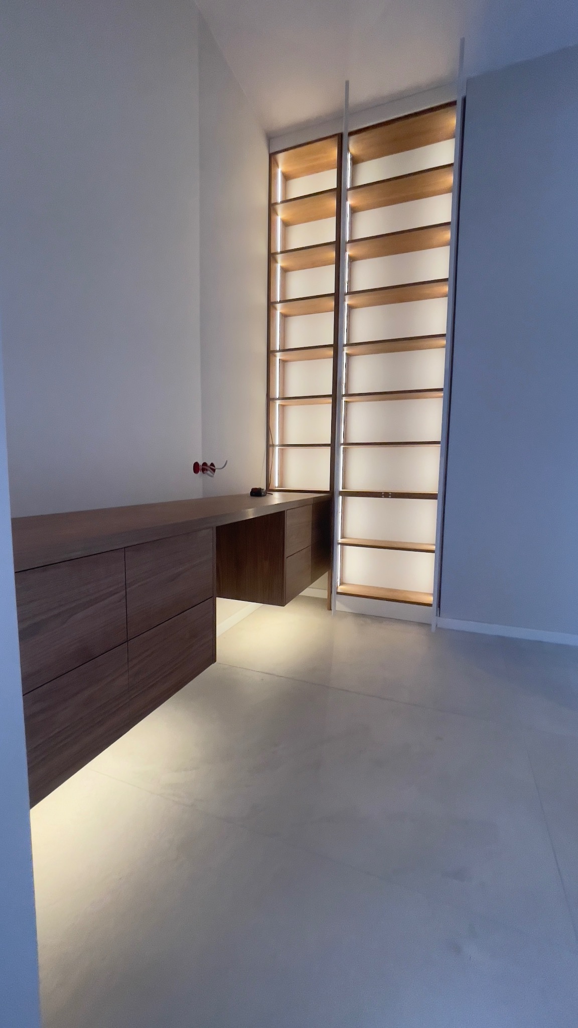 Drewniane biurko z szufladami i regał z podświetlanymi półkami, wykonane na wymiar w Łomiankach, w minimalistycznym wnętrzu.