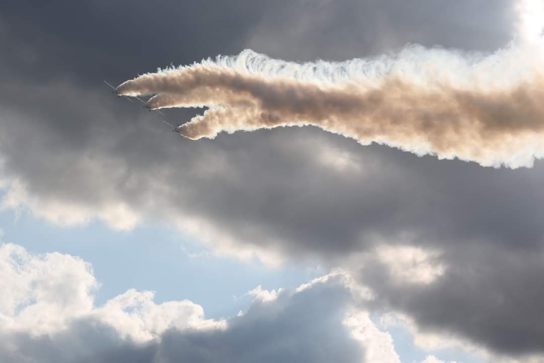 Trzy samoloty w formacji, pozostawiające za sobą smugi dymu na tle zachmurzonego nieba.