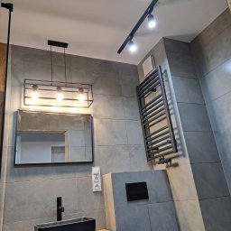 Usługi Remontowo-Budowlane Paweł Majczyna - Nowoczesna łazienka z szarymi płytkami, czarną umywalką nablatową, grzejnikiem drabinkowym i oświetleniem punktowym na suficie.