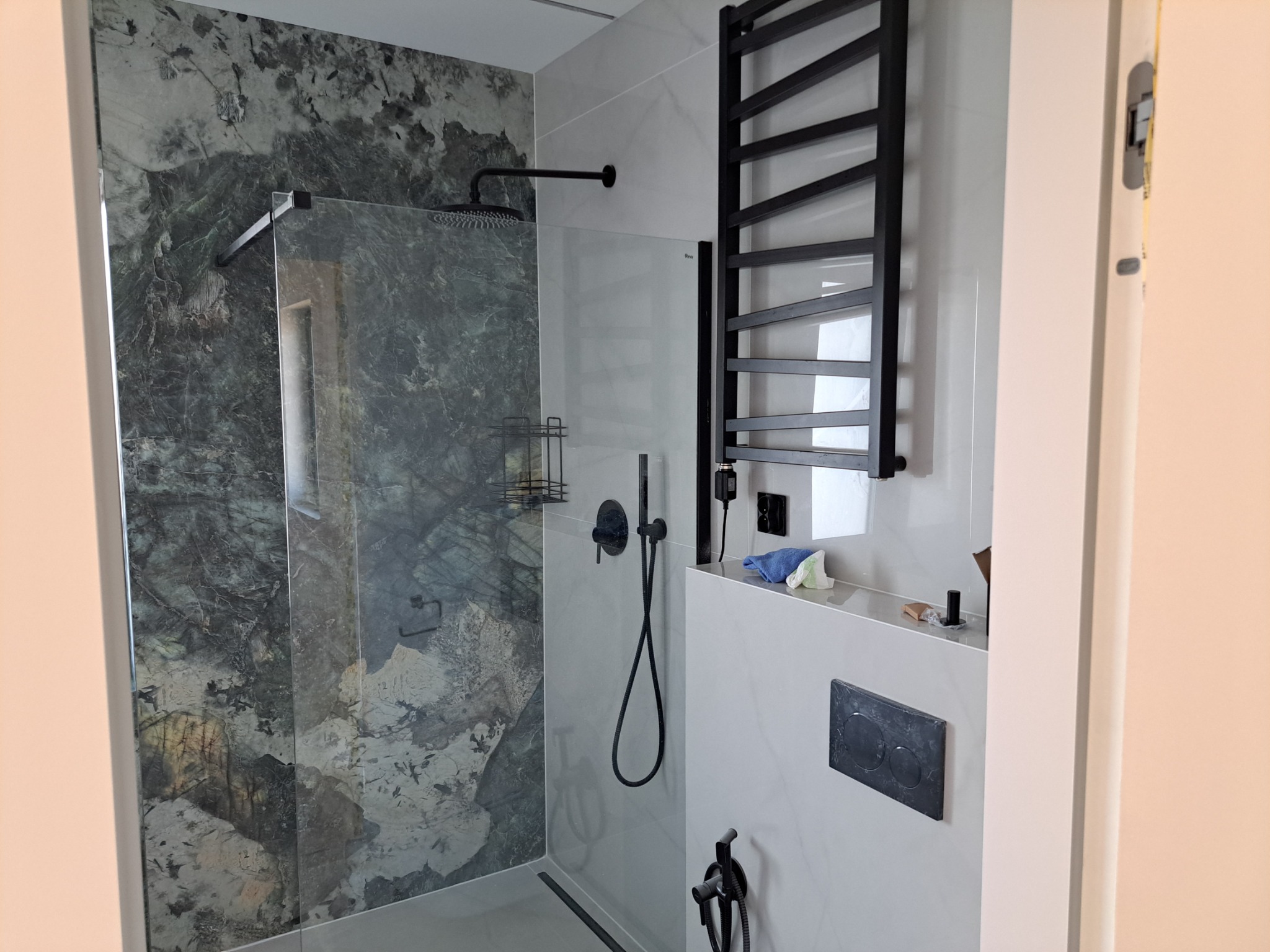 Nowoczesna kabina prysznicowa z panelami imitującymi marmur, czarną armaturą i grzejnikiem drabinkowym, widoczne detale wykończenia.