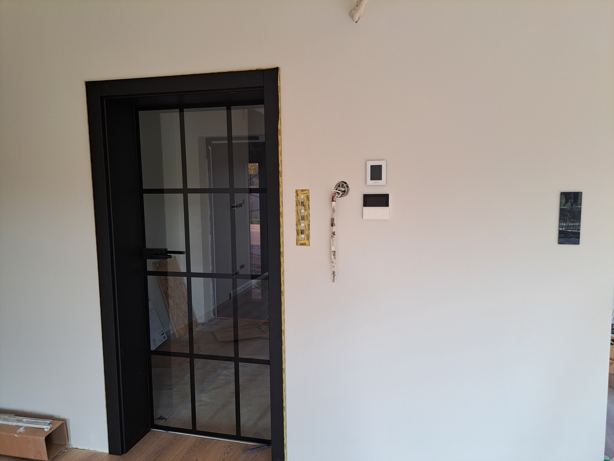 Czarna, przeszklona wewnętrzna stolarka drzwiowa z widocznymi elementami montażowymi na ścianie, w trakcie prac wykończeniowych.