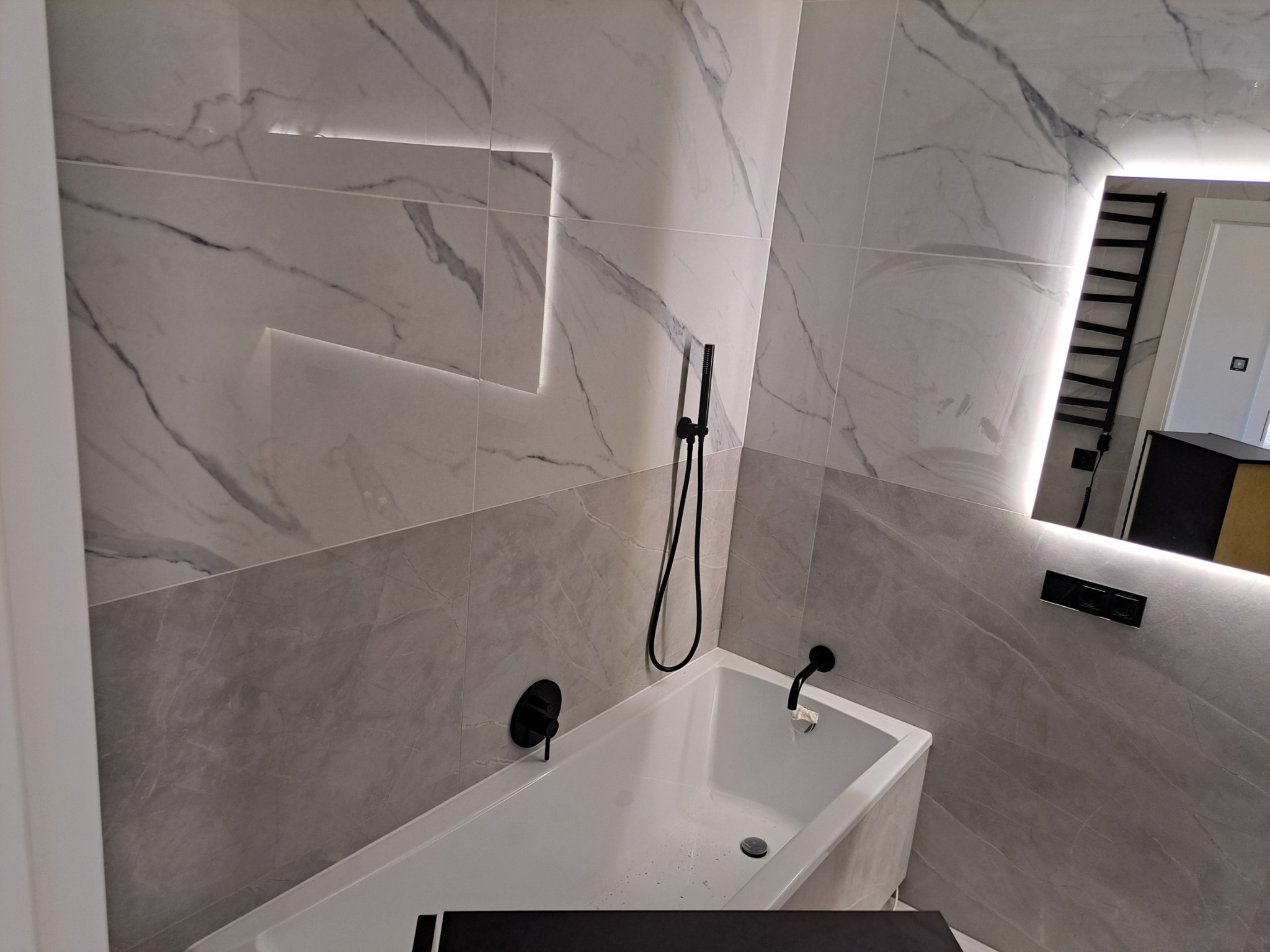 Nowoczesna łazienka z wanną, wykończona płytkami imitującymi marmur z podświetleniem LED, czarna armatura.