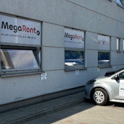 MegaRent.pl - Budynek z oknami z reklamami MegaRent - Multi-Wypożyczalnia Sprzętów i samochód z logo MegaRent na parkingu.
