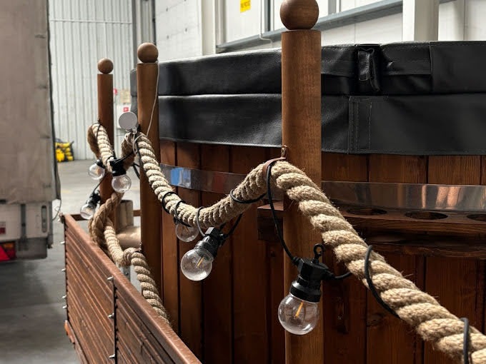 Drewniana balia z oświetleniem sznurkowym i grubym sznurem, widoczna w hali magazynowej z fragmentem naczepy ciężarówki w tle.