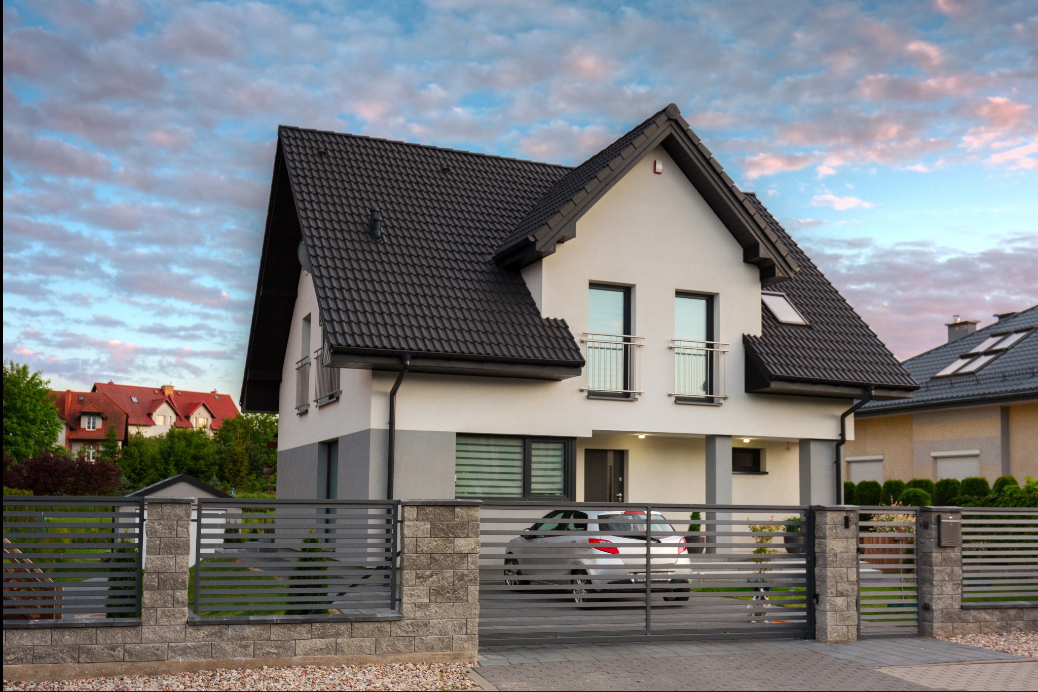 Nowoczesny dom jednorodzinny z szarą, poziomą bramą przesuwną i ogrodzeniem z elementami murowanymi, na tle błękitnego nieba o zmierzchu.