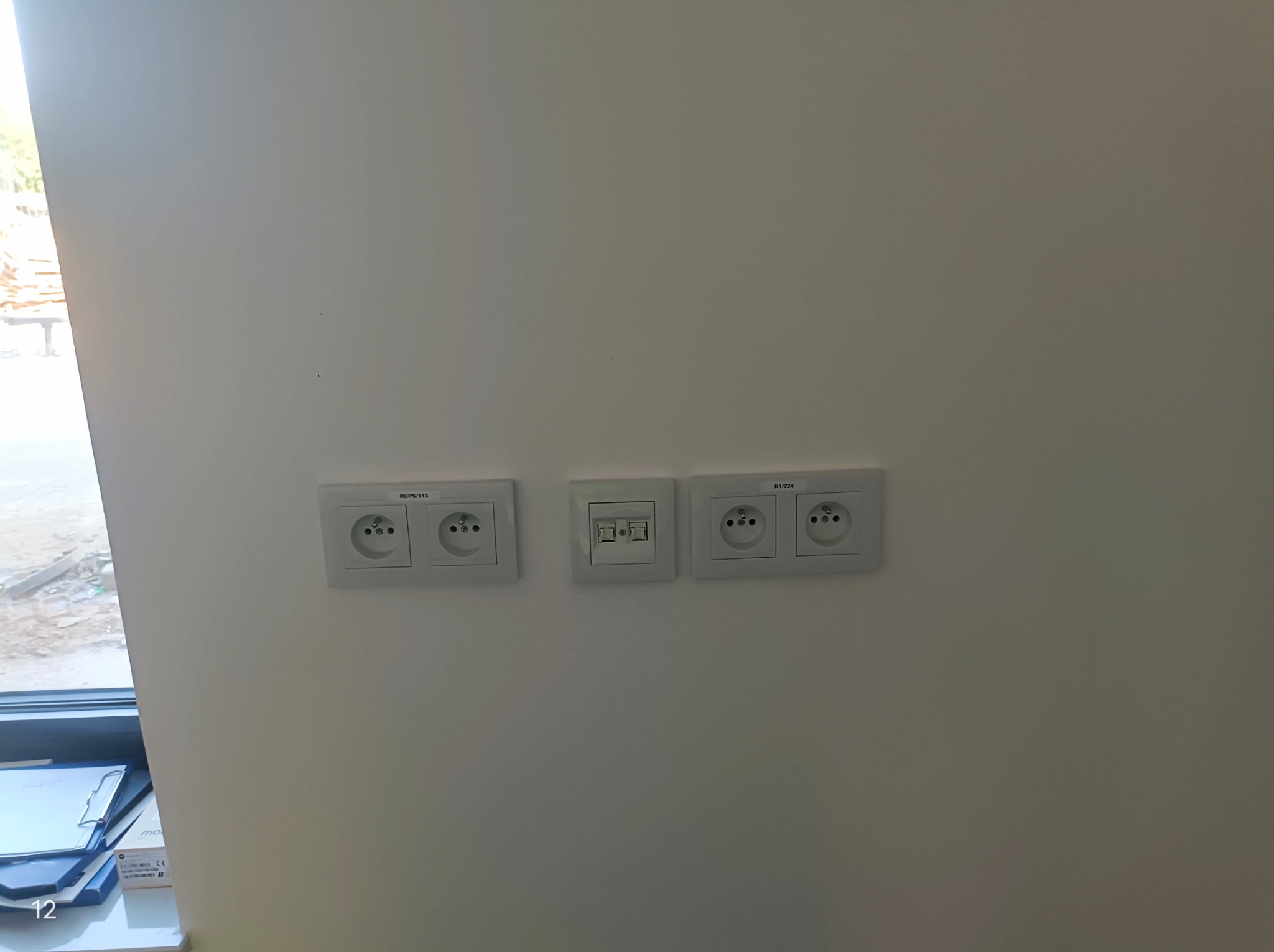 Biała ściana z trzema gniazdkami: dwa podwójne gniazdka elektryczne (RUPS/313 i R1/224) oraz jedno podwójne gniazdko telekomunikacyjne, zamontowane równo, z widocznymi oznaczeniami producenta.