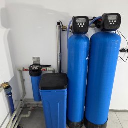 WODEKSPERT - Dwa duże niebieskie filtry wody z cyfrowymi wyświetlaczami, lampa UV, mniejszy filtr wstępny i niebieski zbiornik soli, połączone rurami na tle białej ściany.