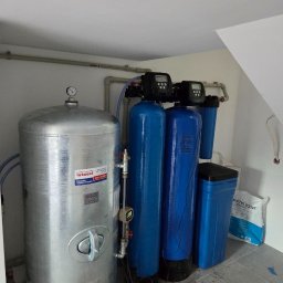 WODEKSPERT - Kompletny system uzdatniania wody z dużym srebrnym zbiornikiem hydroforowym Wimest, dwoma niebieskimi filtrami i zasobnikiem soli, zainstalowany w pomieszczeniu technicznym.