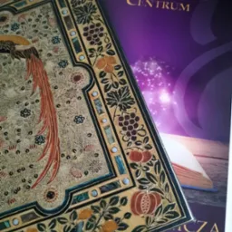 Książka z bogato zdobioną okładką w stylu art nouveau, leżąca na ulotce reklamowej Wydawnictwa Centrum z motywem otwartej książki i magicznego światła.