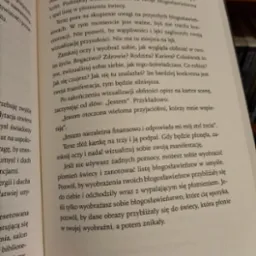 Otwarta książka z fragmentem tekstu o wizualizacji i manifestacji celów, z widocznym fragmentem dłoni z czerwonym paznokciem w lewym dolnym rogu.