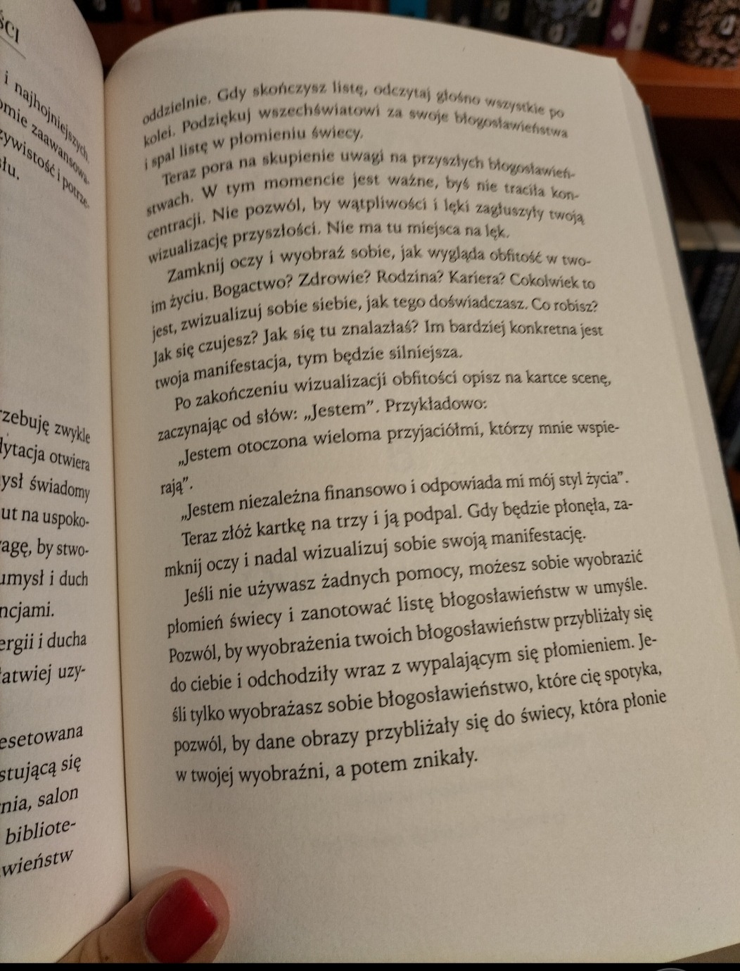 Otwarta książka z fragmentem tekstu o wizualizacji i manifestacji celów, z widocznym fragmentem dłoni z czerwonym paznokciem w lewym dolnym rogu.