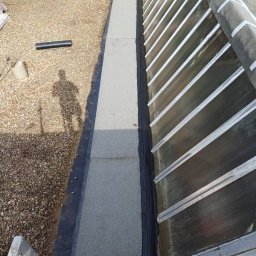 CHIZH GROUP - Widok z góry na fragment dachu z papy w Warszawie, z widoczną nową izolacją i elementami konstrukcyjnymi, cień osoby podczas prac.