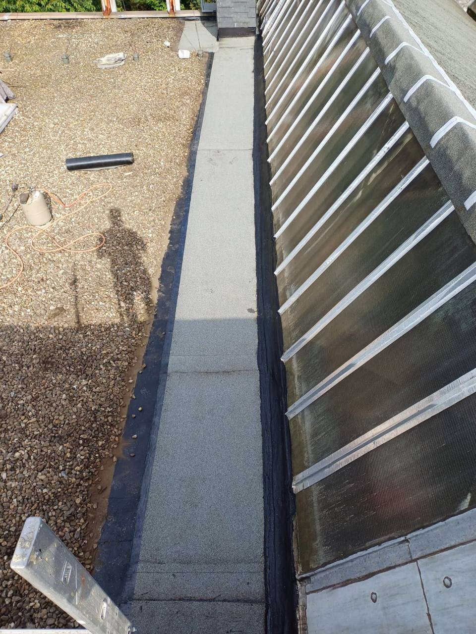 Widok z góry na fragment dachu z papy w Warszawie, z widoczną nową izolacją i elementami konstrukcyjnymi, cień osoby podczas prac.