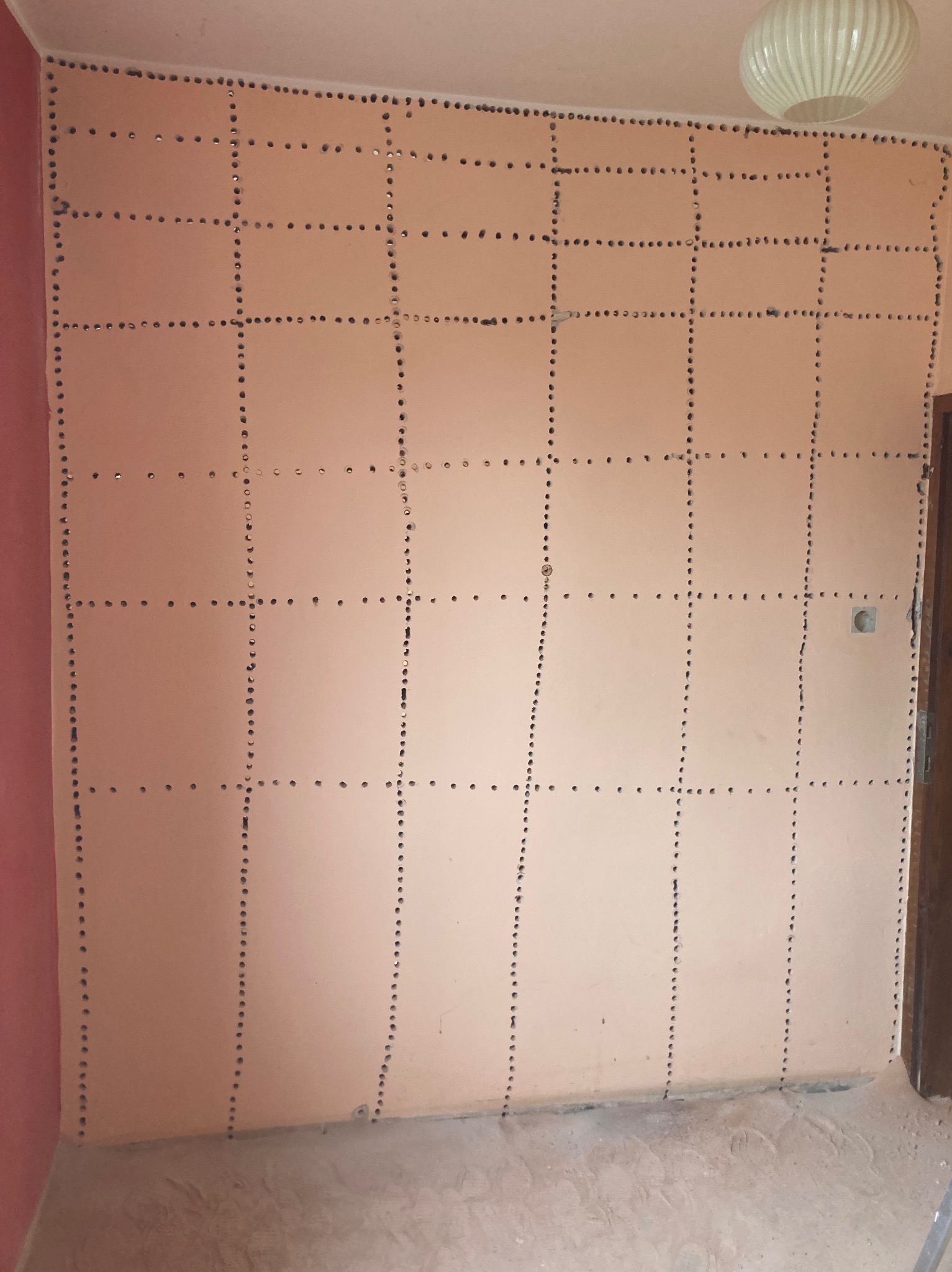 Ściana w pokoju z zaznaczonymi liniami i otworami, przygotowana do dalszych prac wykończeniowych, widoczne elementy instalacji elektrycznej.