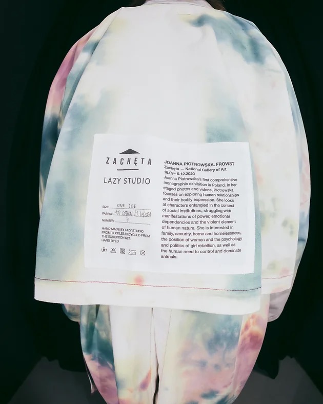 Tył osoby ubranej w ręcznie szytą, barwioną metodą tie-dye kurtkę z metką Zacheta Lazy Studio, wykonaną z recyklingowanych tekstyliów z wystawy Joanny Piotrowskiej.