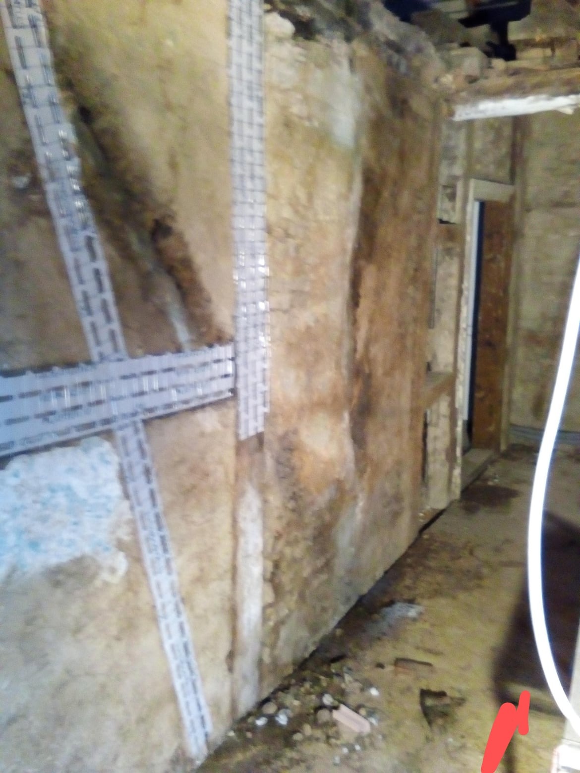 Przygotowanie ściany do gładzi: surowa ściana z widocznymi fragmentami starego tynku, wzmocniona metalową siatką mocowaną na klej gipsowy, widoczne ślady wilgoci.