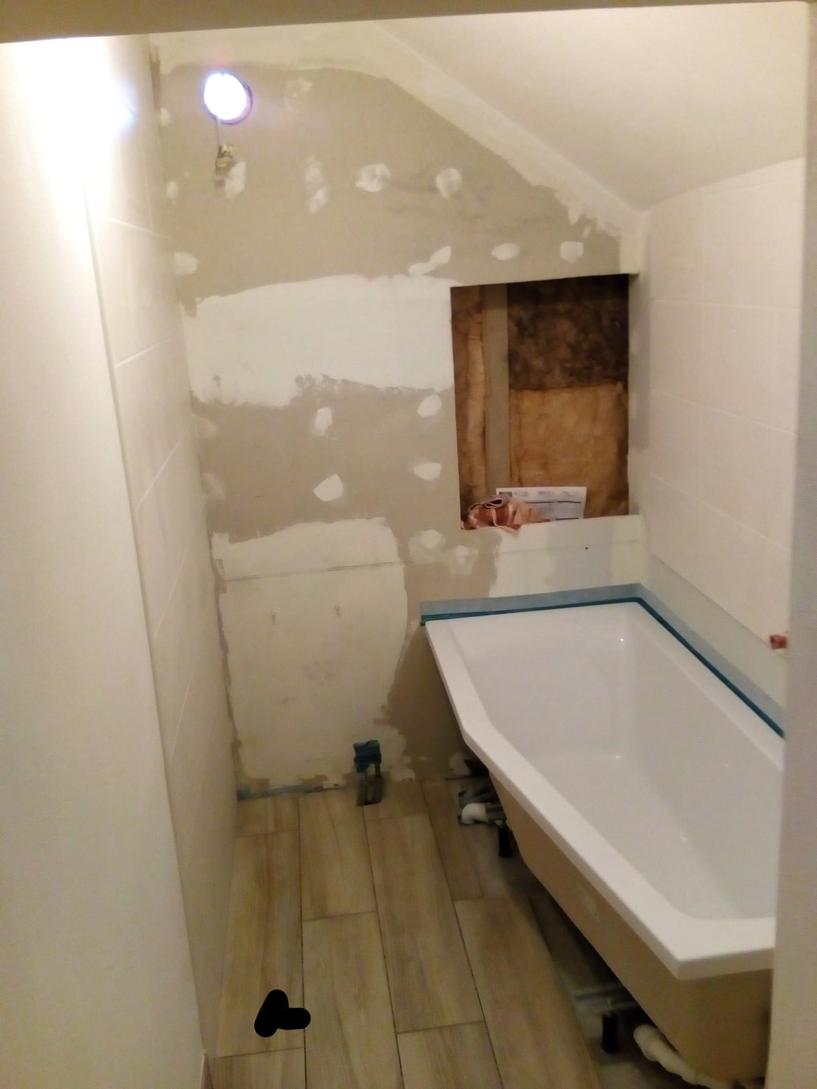 Łazienka w trakcie prac wykończeniowych: częściowo położone płytki na ścianach, surowa ściana z widocznymi łatami gipsu, zamontowana wanna z zabezpieczeniem krawędzi, płytki podłogowe na podłodze...