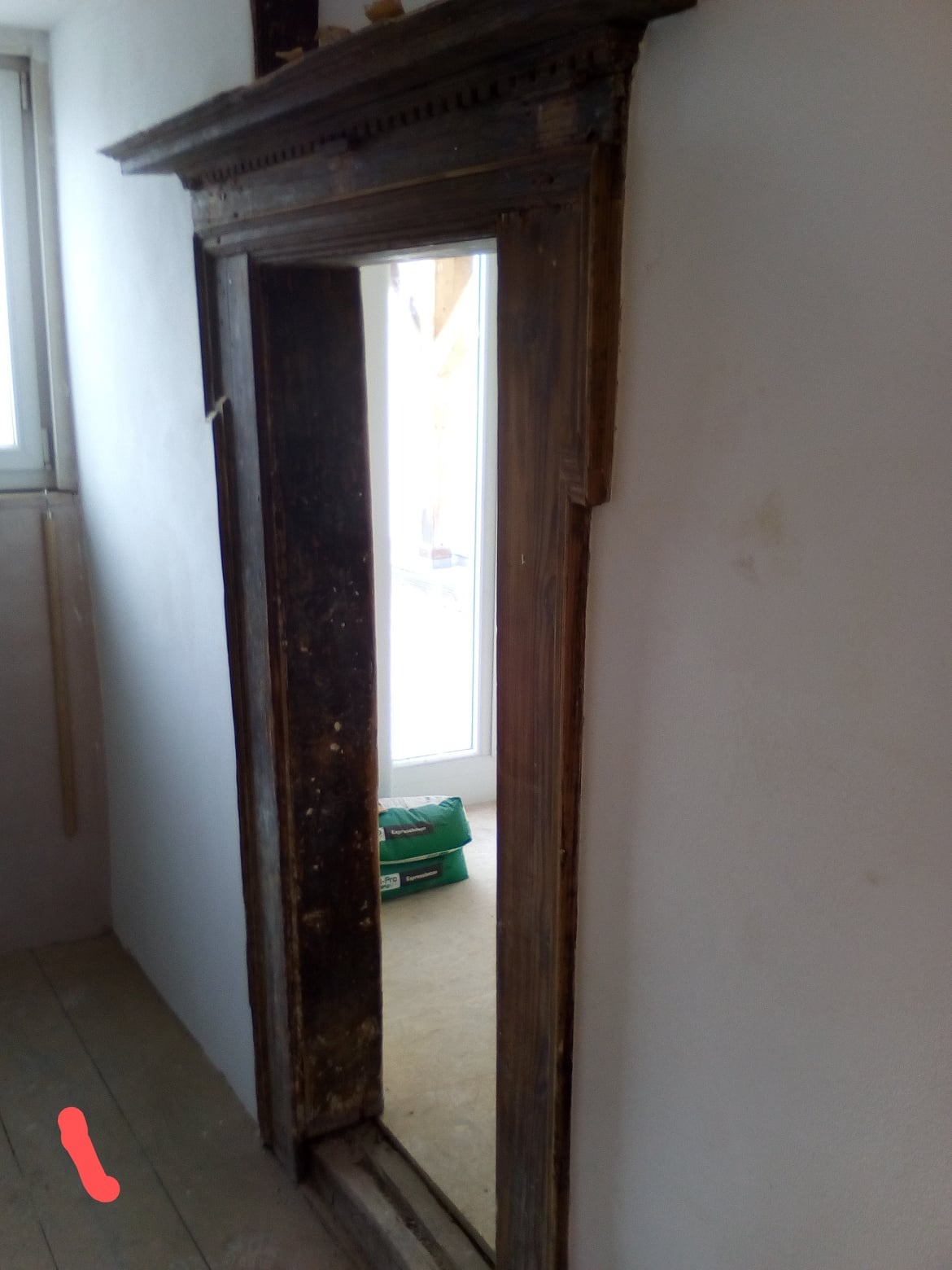 Stara, drewniana framuga drzwiowa z dekoracyjnymi elementami, widoczne worki z zaprawą w tle, ściany w trakcie przygotowania do malowania.