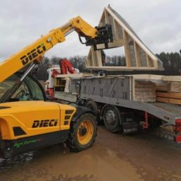 Cezary Gerek - Żółta ładowarka teleskopowa Dieci podnosi element konstrukcyjny dachu domu szkieletowego z ciężarówki na placu budowy.