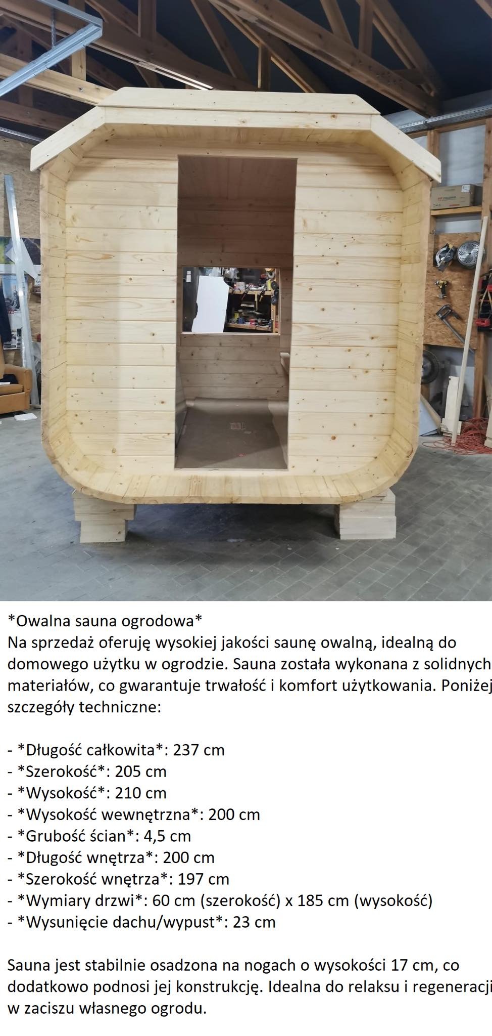 Owalna sauna ogrodowa z jasnego drewna, widoczna z przodu, z wyraźnym wejściem, umieszczona na drewnianych podporach w warsztacie.