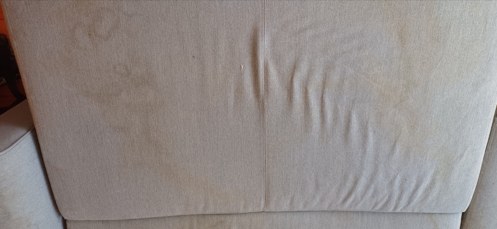 Fragment beżowej kanapy z widocznymi plamami i zagnieceniami na tapicerce.