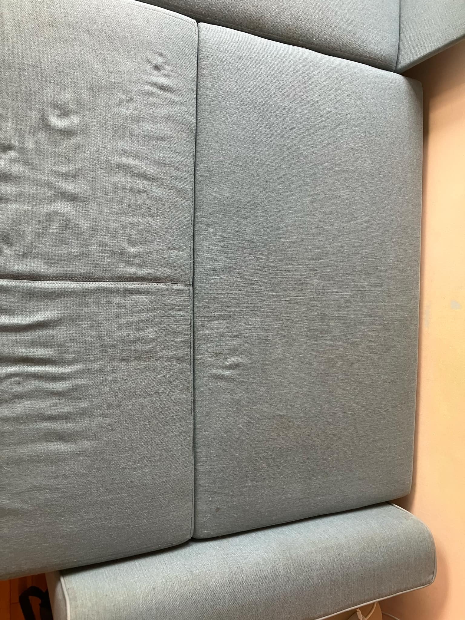 Fragment sofy z jasnoniebieską tapicerką z widocznymi plamami i zabrudzeniami przed czyszczeniem.