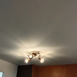 Gładki, pomalowany na szaro sufit z zamontowaną, nowoczesną lampą sufitową z trzema reflektorami, oświetlającymi przestrzeń.