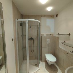 Mateusz Rzepa - Jasna łazienka po remoncie: kabina prysznicowa z chromowaną armaturą, toaleta i umywalka. Beżowe płytki na ścianach i podłodze. Oświetlenie sufitowe.