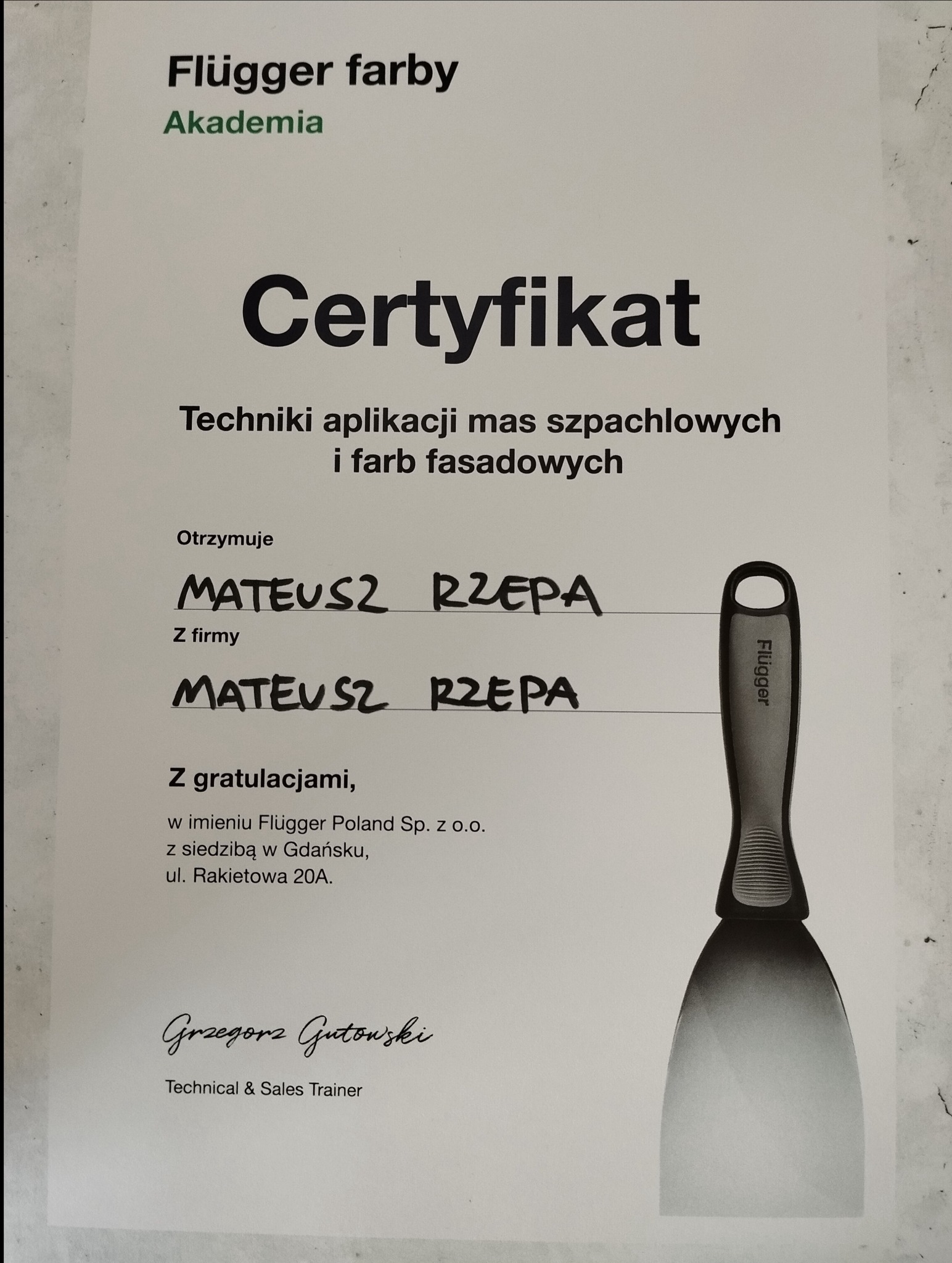 Certyfikat ukończenia szkolenia z technik aplikacji mas szpachlowych i farb fasadowych marki Flügger, z ilustracją szpachelki. Dokument potwierdzający kwalifikacje.