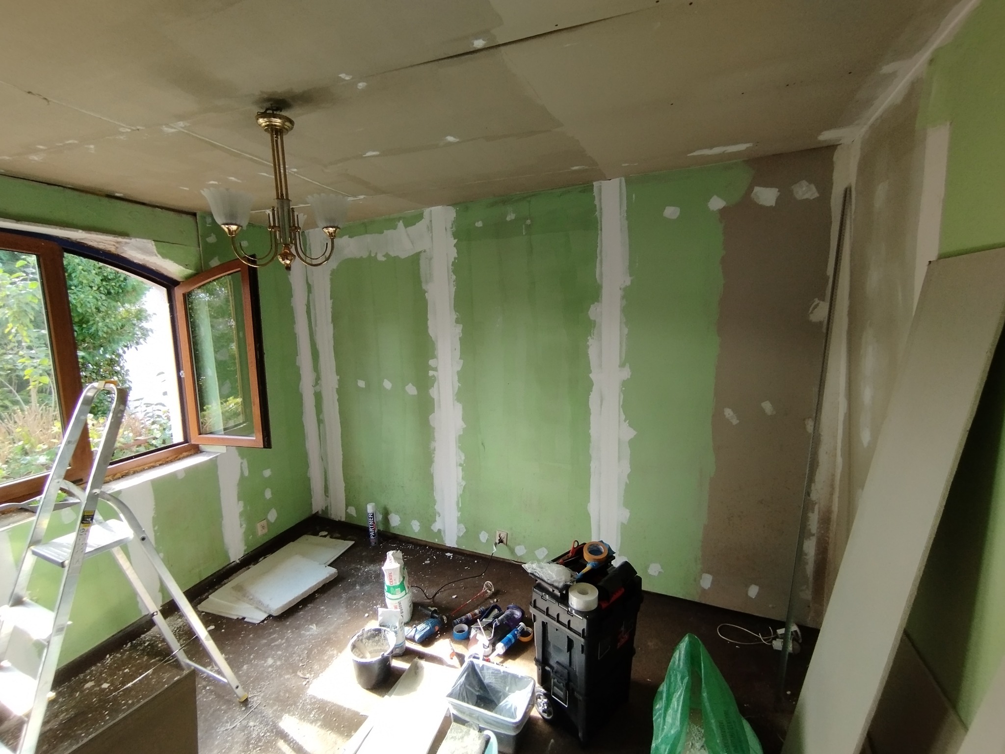 Pokój w trakcie prac wykończeniowych w Rumii. Widoczne ściany przygotowane do dalszych prac, narzędzia i drabina. Ściany częściowo pomalowane na zielono.