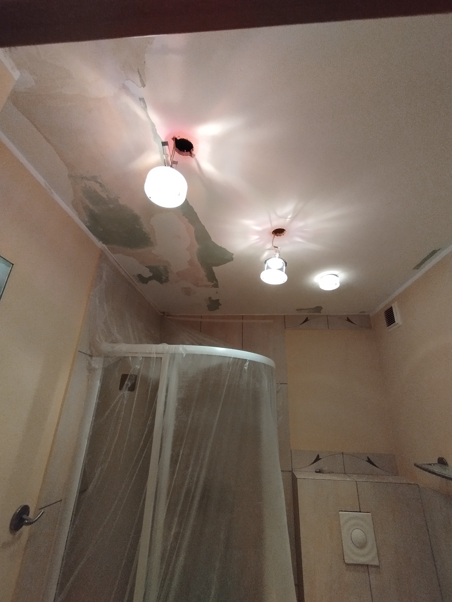 Łazienka w trakcie remontu: widoczne uszkodzenia na suficie, zabezpieczona kabina prysznicowa folią malarską, przygotowania do prac wykończeniowych.