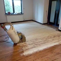 Usługi budowlane Grzegorz Ornawka - Cyklinowanie drewnianej podłogi w trakcie renowacji, widoczna maszyna do cyklinowania Janzer i fragment podłogi przed i po cyklinowaniu.