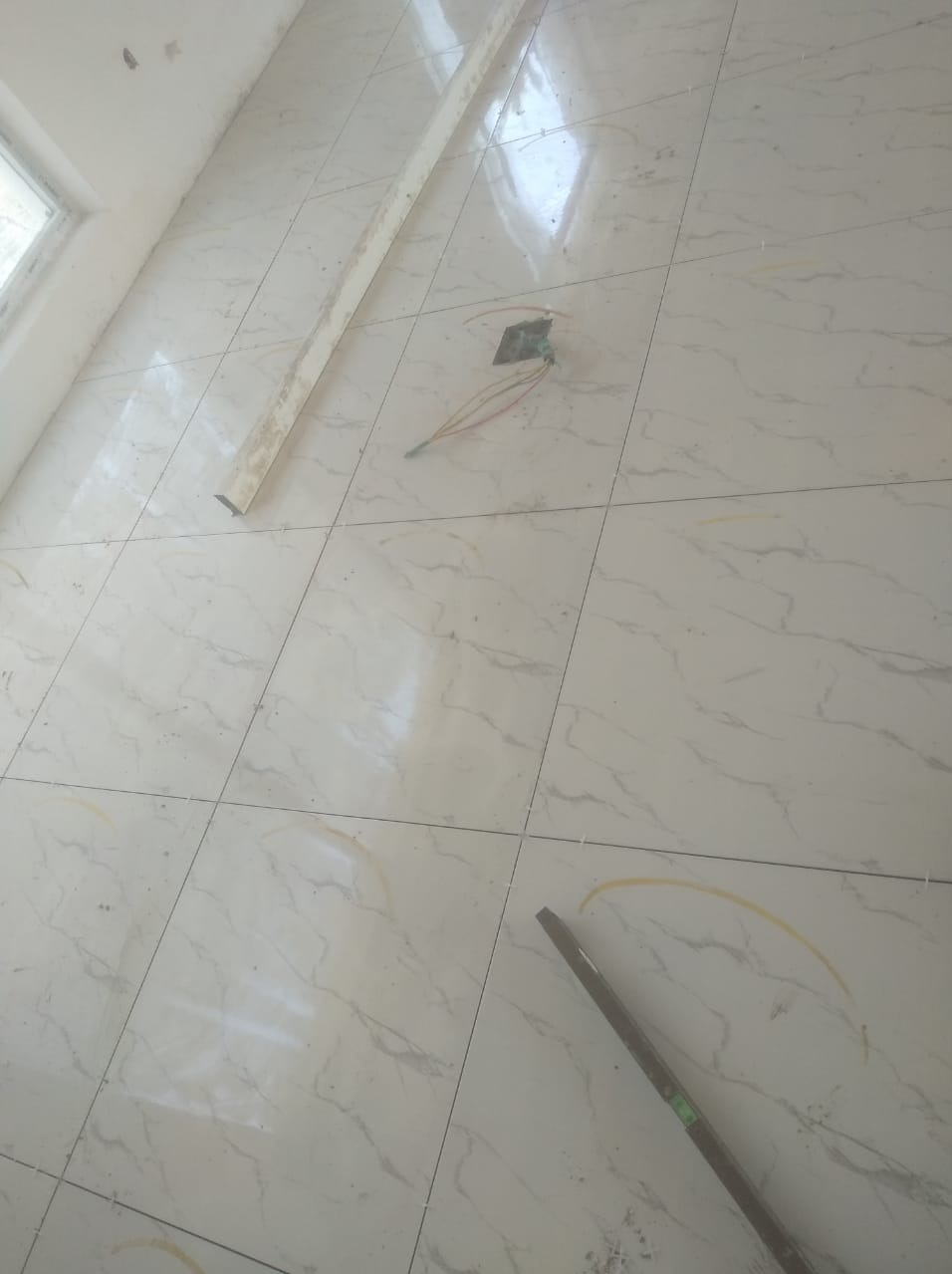 Białe, marmurkowe płytki podłogowe w trakcie montażu, widoczne krzyżyki dystansowe, listwa przypodłogowa i puszka elektryczna z wystającymi przewodami.
