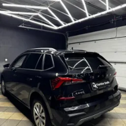 Czarny samochód Skoda Kamiq z przyciemnionymi szybami, zaparkowany w oświetlonym garażu z logo DarkKar Studio na tylnej klapie.
