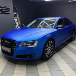 Niebieski Audi A8 po oklejeniu folią matową w studiu detailingowym, widoczne detale wykończenia i oświetlenie LED w tle.