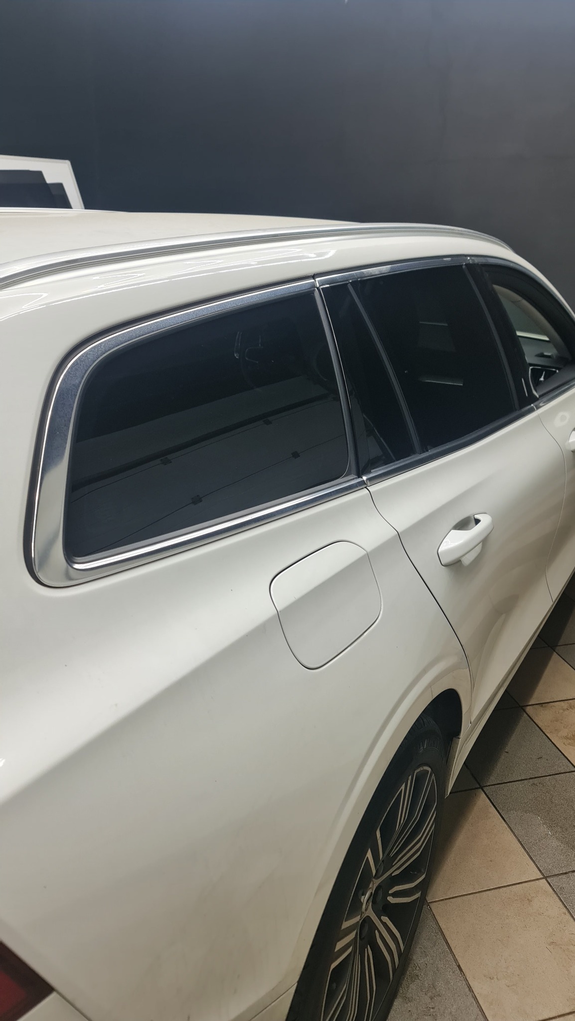 Białe kombi z przyciemnionymi tylnymi szybami, widoczne z boku na tle ciemnej ściany.