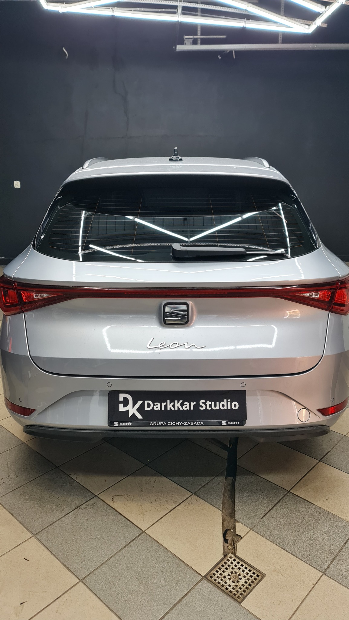 Srebrny samochód Seat Leon, widok z tyłu, zaparkowany w studiu detailingowym DarkKar Studio, oświetlony lampami, z widocznym odpływem w podłodze.