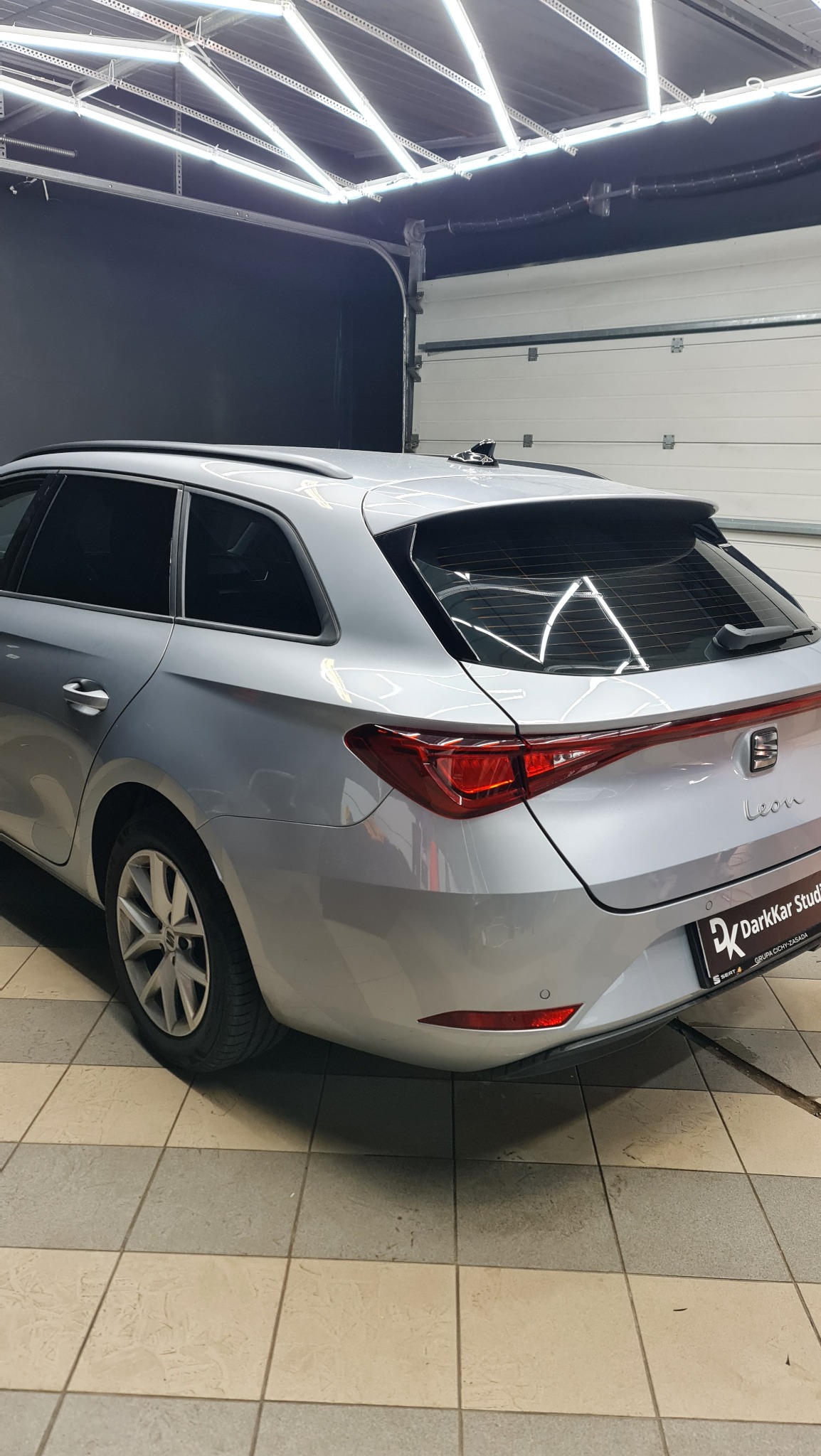 Srebrne kombi Seat Leon z przyciemnionymi tylnymi szybami, zaparkowane w dobrze oświetlonym garażu z podłogą w szachownicę. Widoczny znak firmowy DarkKar Studio na tylnej klapie.