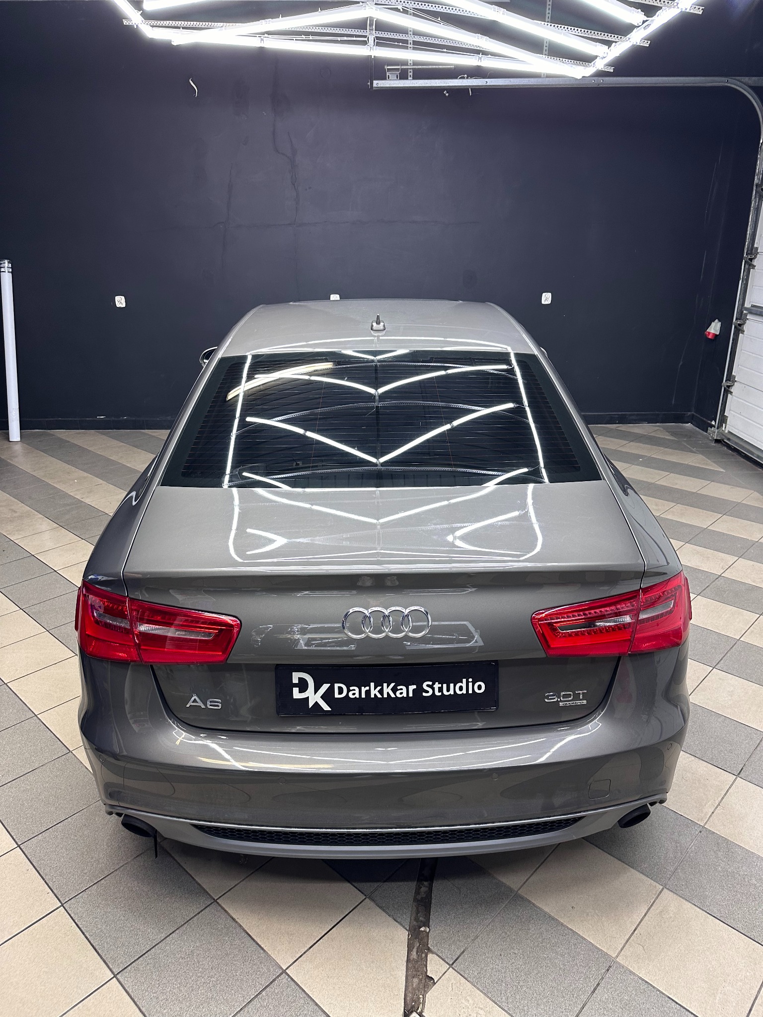 Szary samochód Audi A6 z przyciemnionymi szybami, widoczny od tyłu, zaparkowany w studiu w Poznaniu. Na tylnej klapie widoczne logo firmy DarkKar Studio.