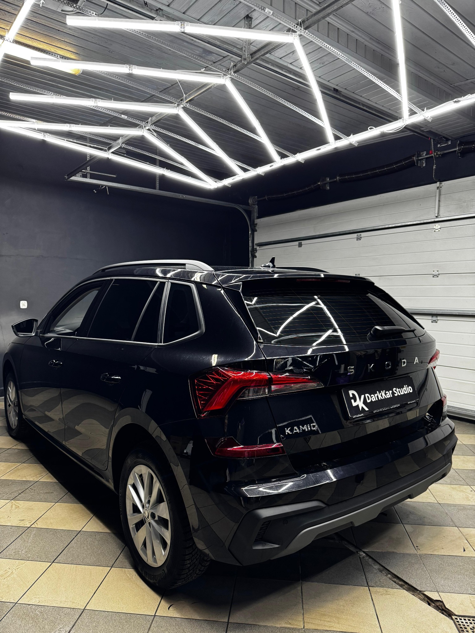 Czarny samochód Skoda Kamiq z przyciemnionymi szybami, zaparkowany w oświetlonym garażu z logo DarkKar Studio na tylnej klapie.