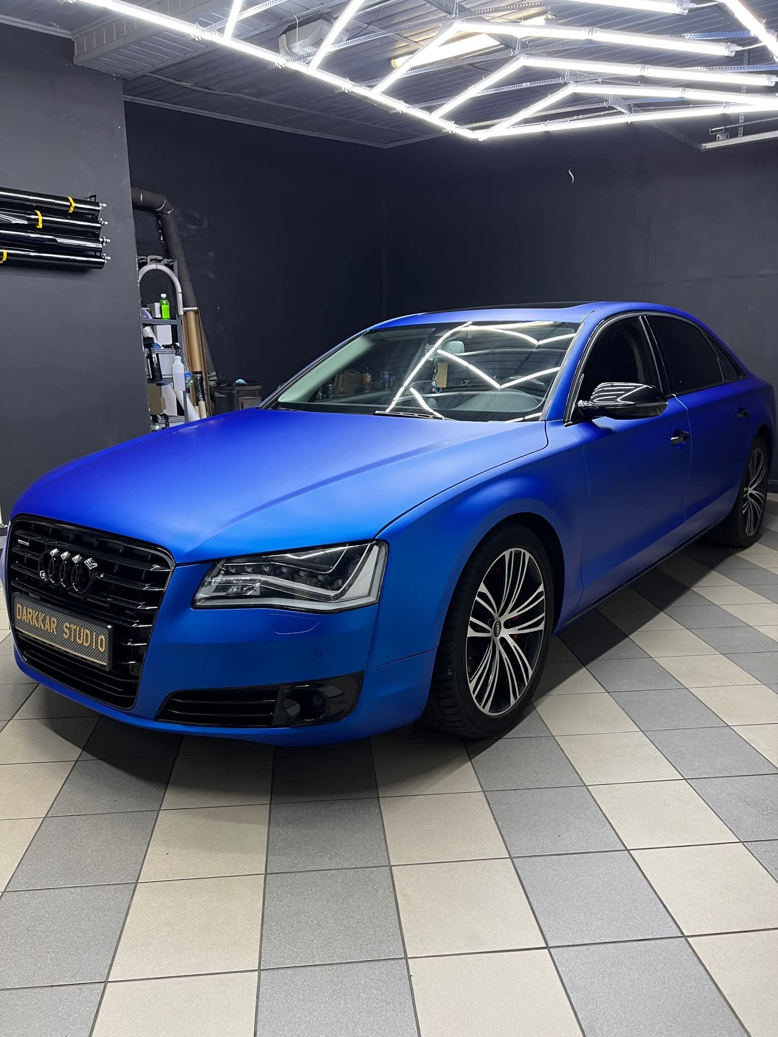 Niebieski Audi A8 po oklejeniu folią matową w studiu detailingowym, widoczne detale wykończenia i oświetlenie LED w tle.