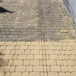 Częściowo wyczyszczona, beżowa kostka brukowa na podjeździe, widoczna różnica w kolorze między czystą a brudną powierzchnią.