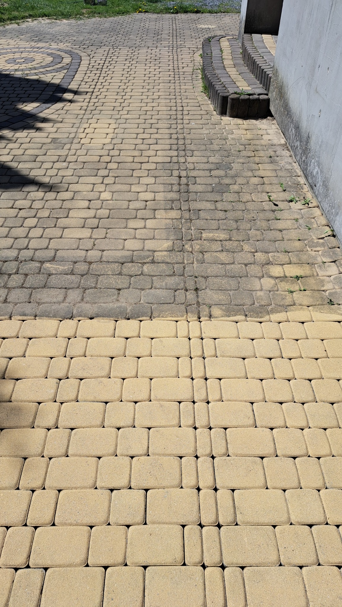 Częściowo wyczyszczona, beżowa kostka brukowa na podjeździe, widoczna różnica w kolorze między czystą a brudną powierzchnią.