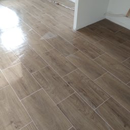 STYL-BUD KAZIMIERZ M - Ułożona podłoga z płytek imitujących drewno w jasnym pomieszczeniu. Widoczne kable elektryczne przy ścianie. Nowoczesny wzór, świeżo po remoncie.
