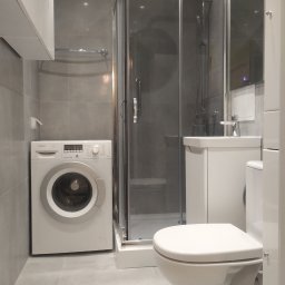 STYL-BUD KAZIMIERZ M - Nowoczesna łazienka w szarościach z kabiną prysznicową, umywalką z szafką i pralką Bosch. Minimalistyczny design, jasne oświetlenie, płytki ceramiczne na ścianach i podłodze.
