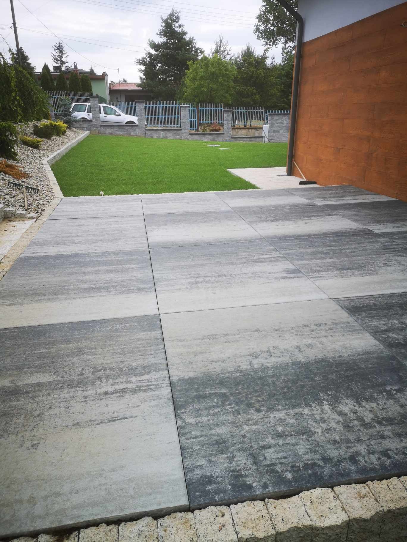 Ułożona szara kostka brukowa na posesji, widok na trawnik i ogrodzenie. Nowoczesny design, regularny wzór. Estetyczne wykończenie przestrzeni zewnętrznej.