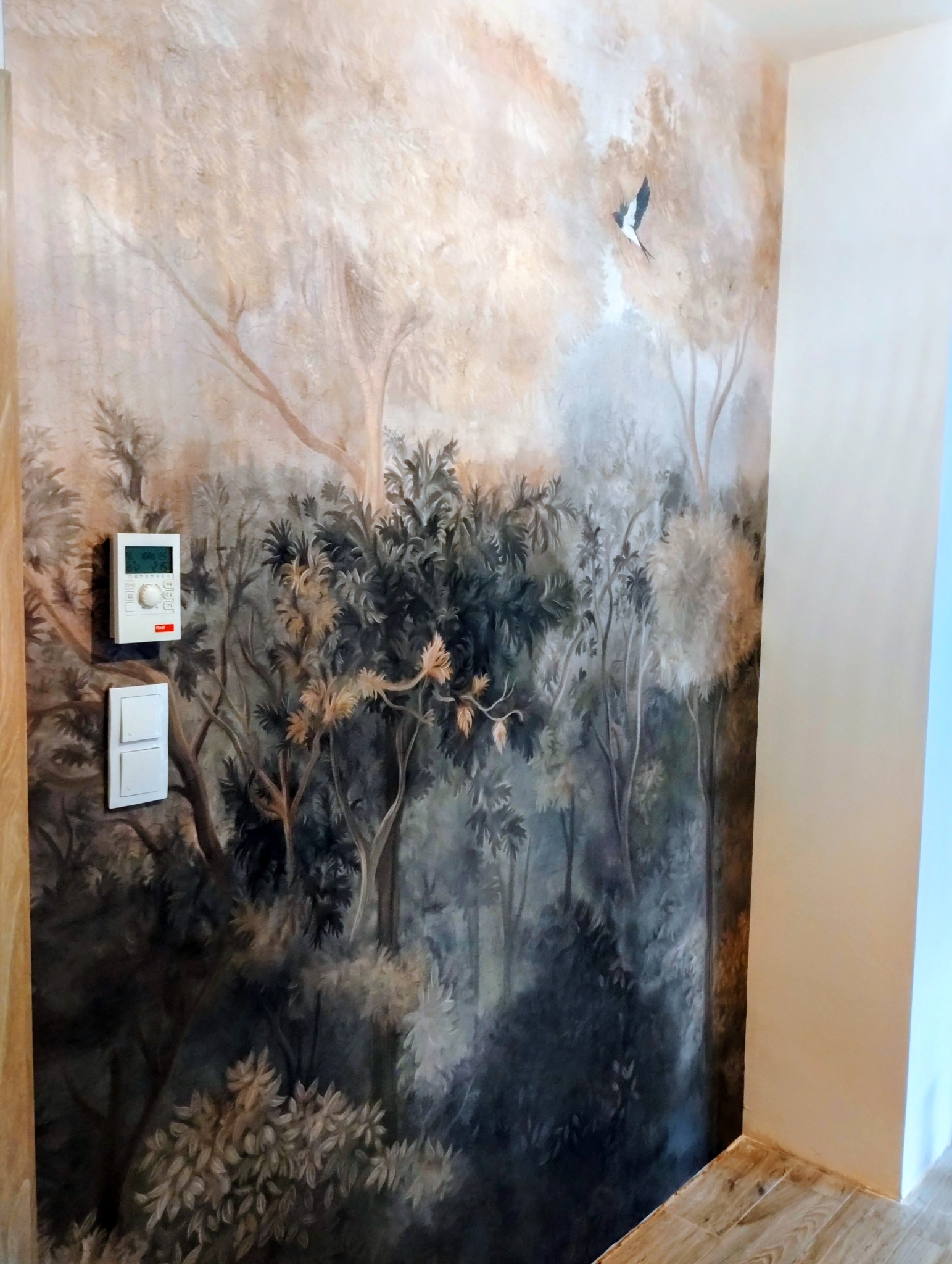 Malowidło ścienne w stylu leśnym z motywem ptaka, regulator temperatury i włącznik światła na ścianie. Wykończenie wnętrza z artystycznym akcentem.