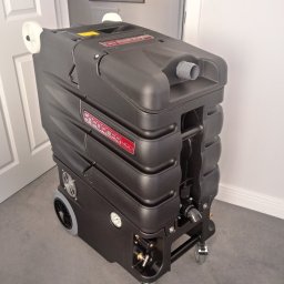 Łowcy Porządku - Firma Sprzątająca - Profesjonalny, czarny odkurzacz piorący Enforcer 400 na kółkach, stojący na szarym dywanie w pomieszczeniu z białymi drzwiami i ścianami.